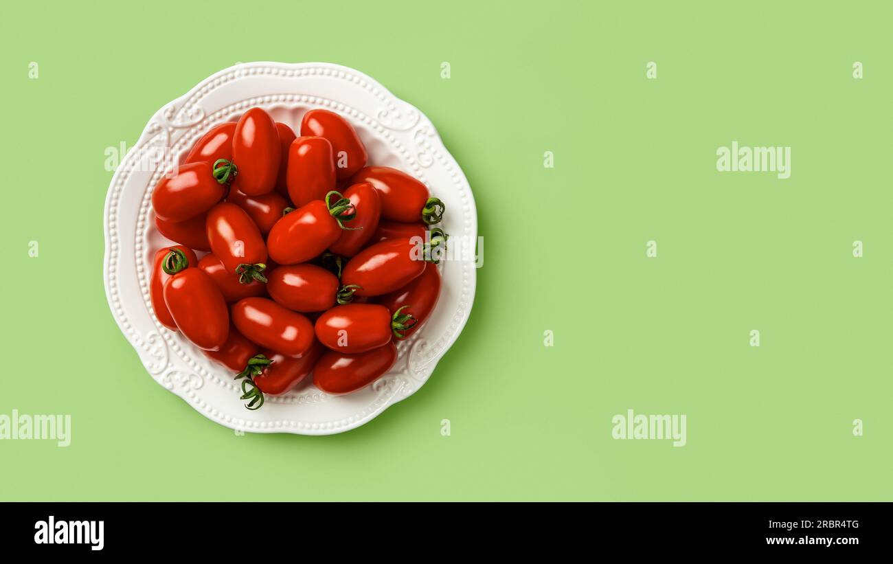 Red Ornela cherry tomatoes on a white plate over green background. Heap of small bottle shaped tomatoes on a plate. Organic vegetables vegetarian food Stock Photo