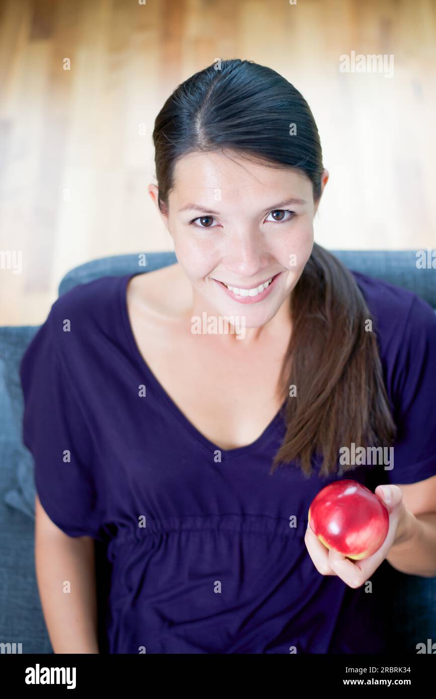 High angle view of a beautiful smiling young woman showing a fresh juicy red apple in her hand as she promotes a healthy organic diet Stock Photo