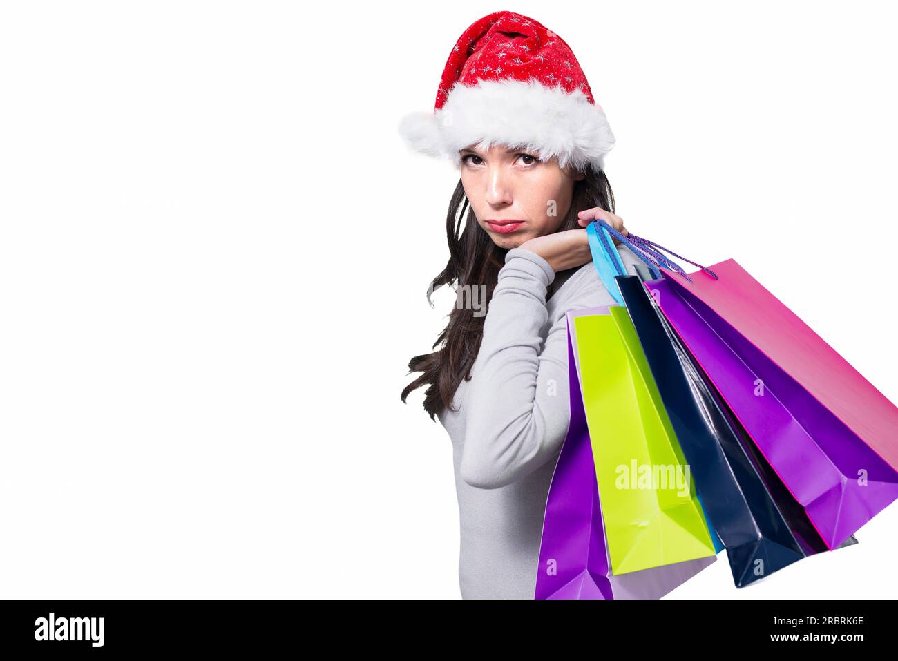 Pretty young woman in a Santa hat standing sulking with a sad face while out Christmas shopping with a handful of colourful shopping bags as she Stock Photo