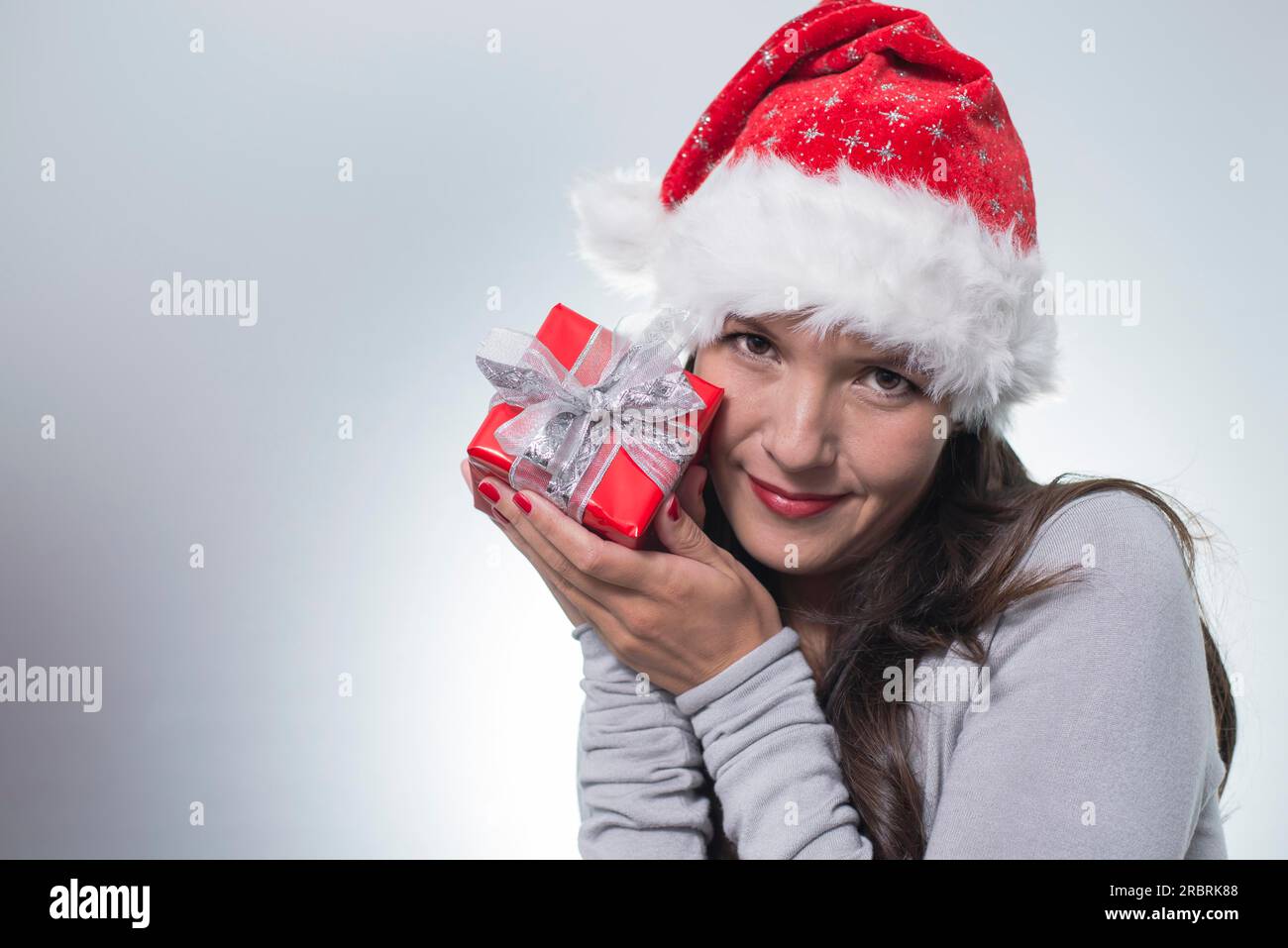 Beautiful woman in a red santa hat holding a gift-wrapped present to ...