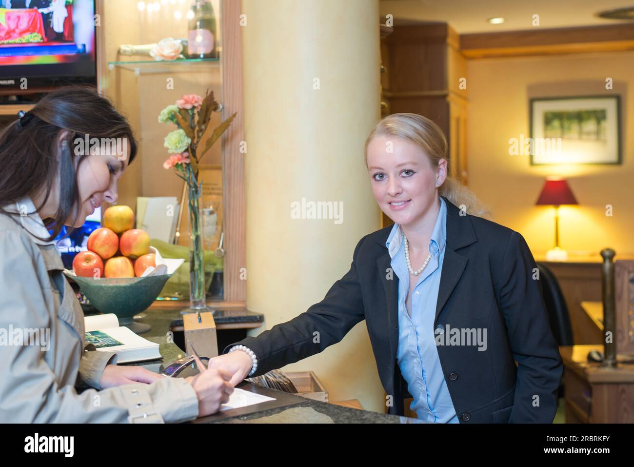 Smiling attractive young receptionist helping a hotel guest check in pointing to information on the form that needs to be completed as they stand at Stock Photo