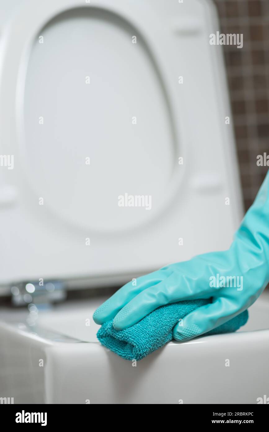 Hand of a person cleaning the toilet seat in rubber gloves with a