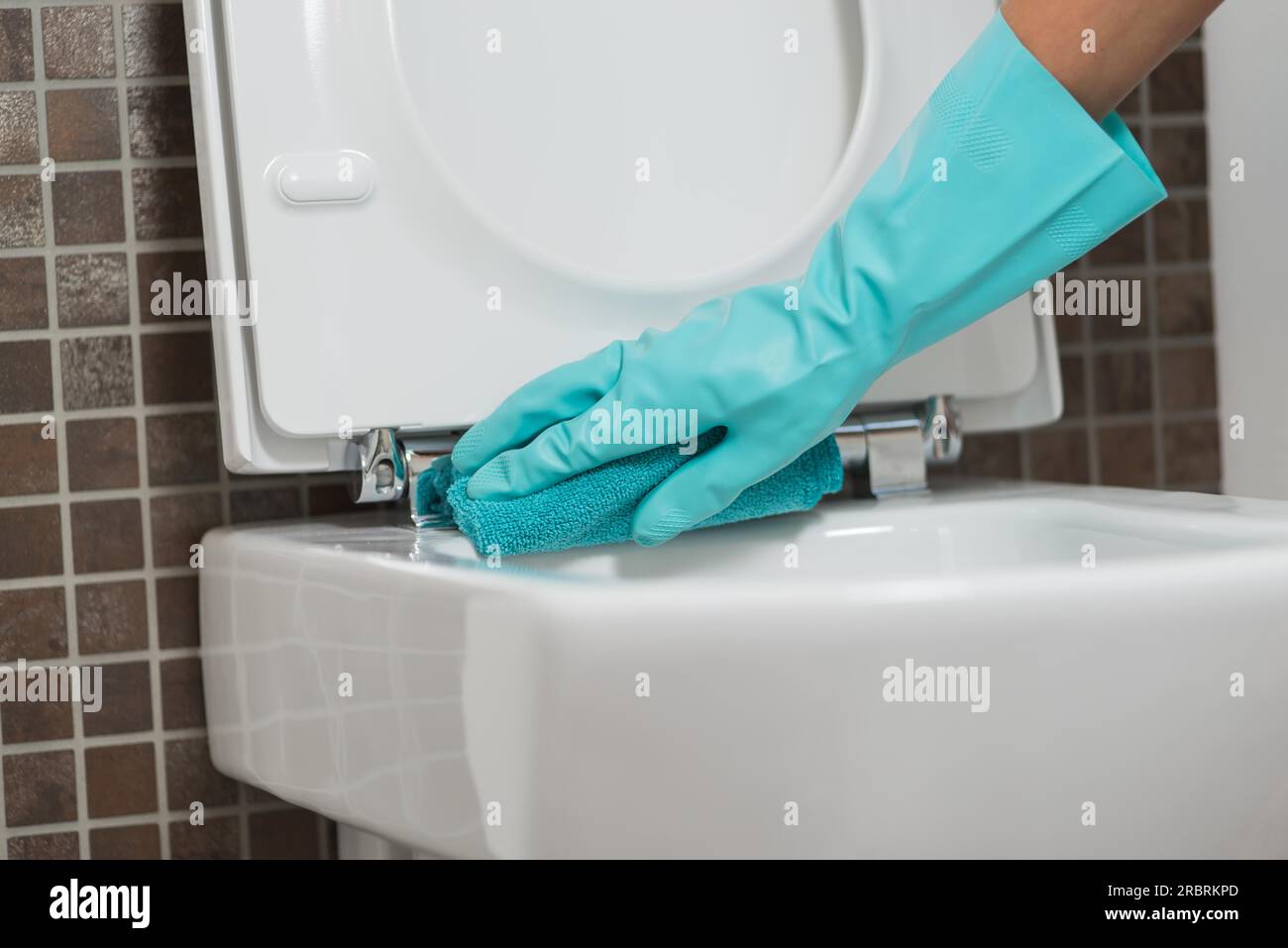 Hand of a person cleaning the toilet seat in rubber gloves with a