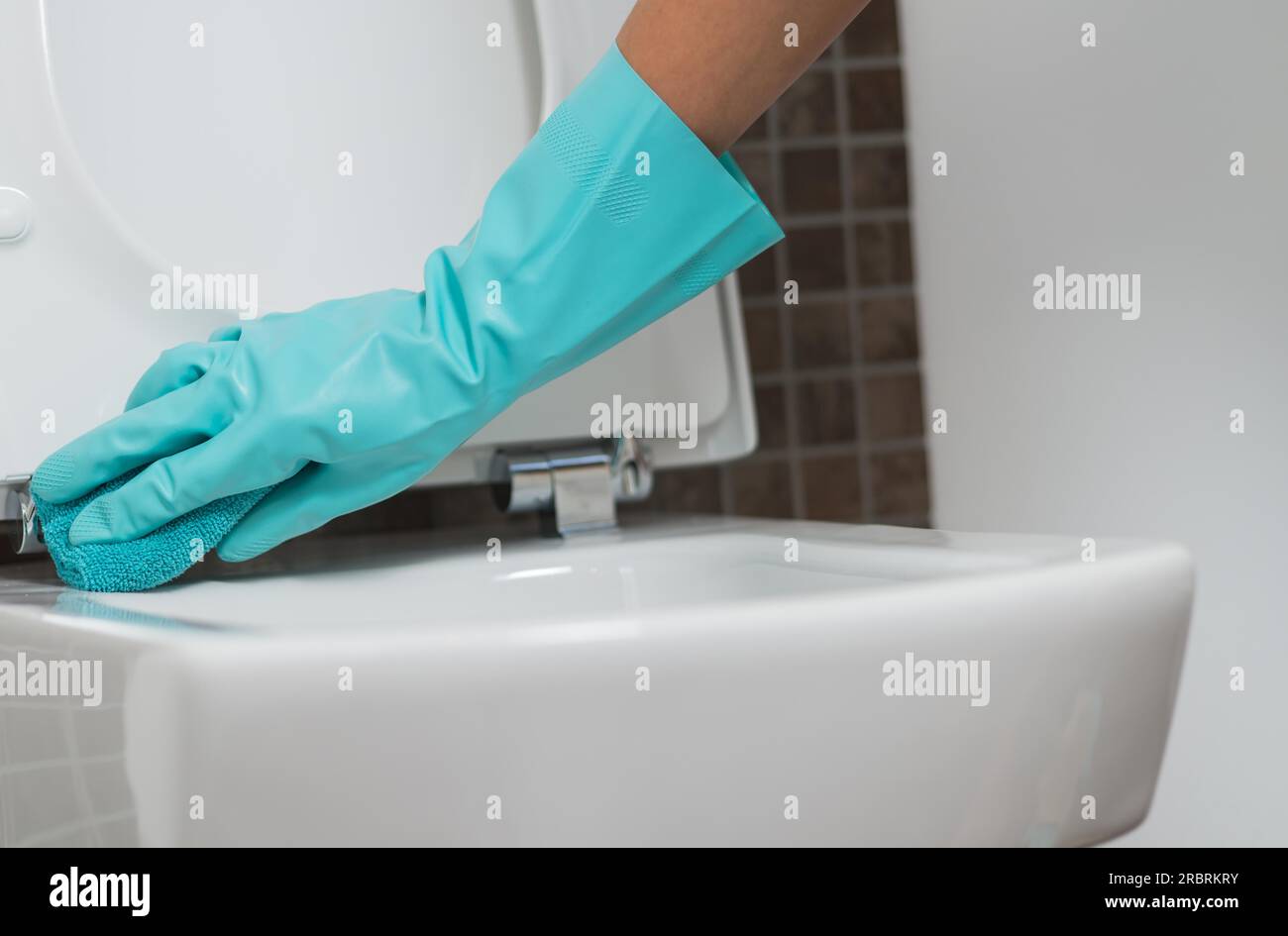 Hand of a person cleaning the toilet seat in rubber gloves with a