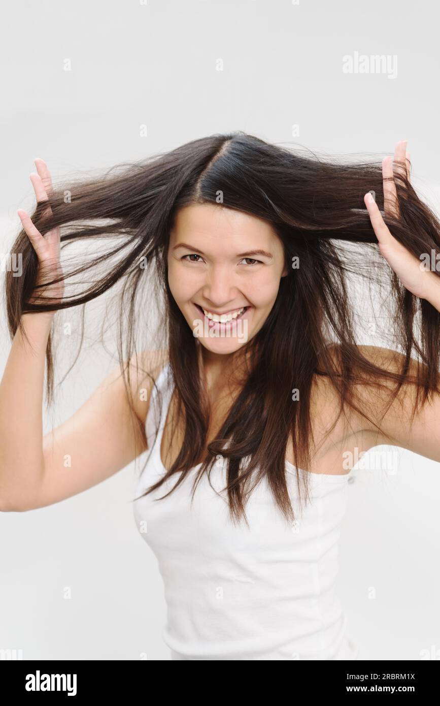 Joyful beautiful young woman playing with her long brunette hair running her fingers through the tresses as she lifts it away from her head while Stock Photo