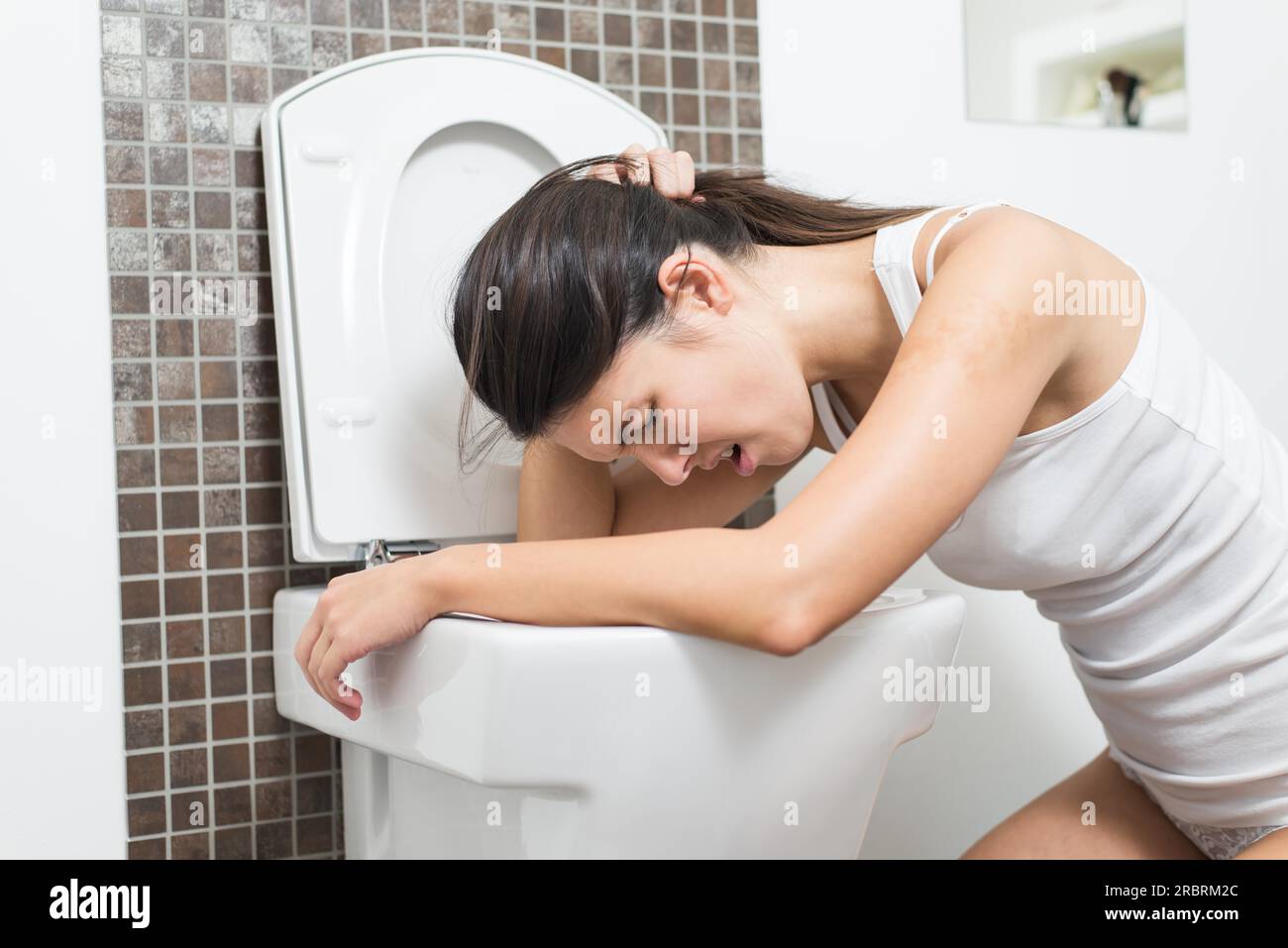 Young woman vomiting into the toilet bowl in the early stages of pregnancy or after a night of partying and drinking Stock Photo