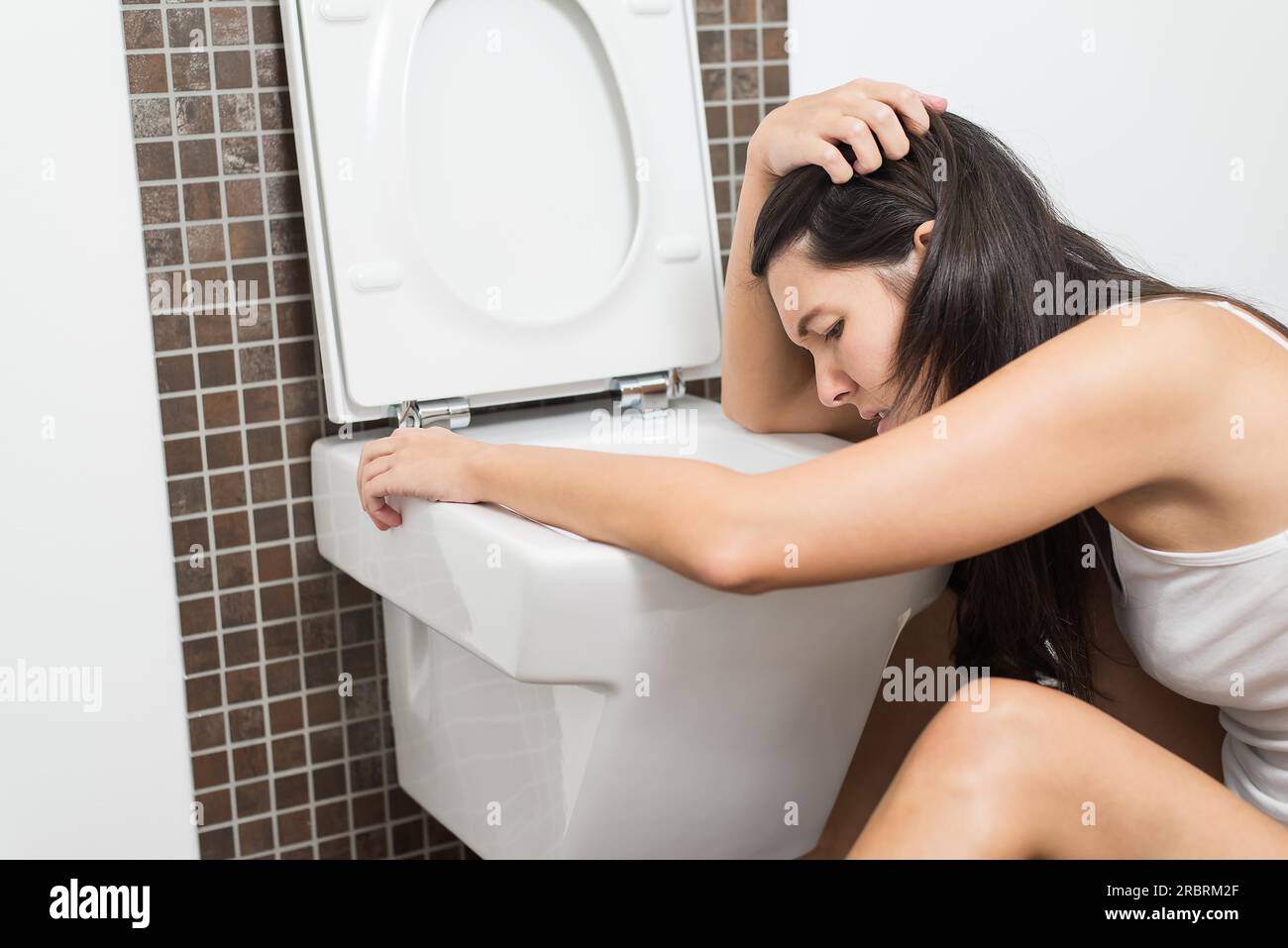 Young woman vomiting into the toilet bowl in the early stages of pregnancy or after a night of partying and drinking Stock Photo