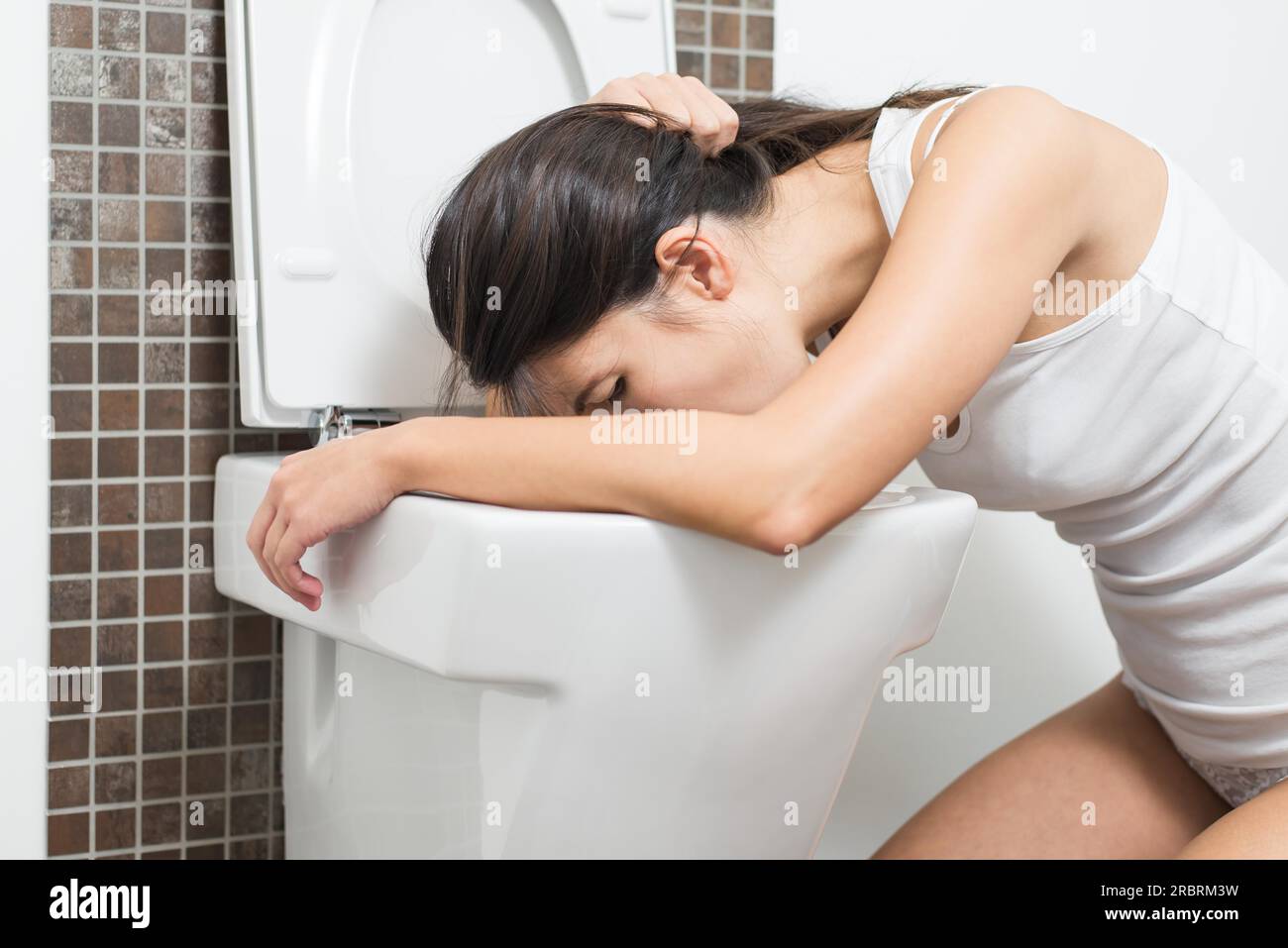Young woman vomiting into the toilet bowl in the early stages of pregnancy or after a night of partying and drinking Stock Photo