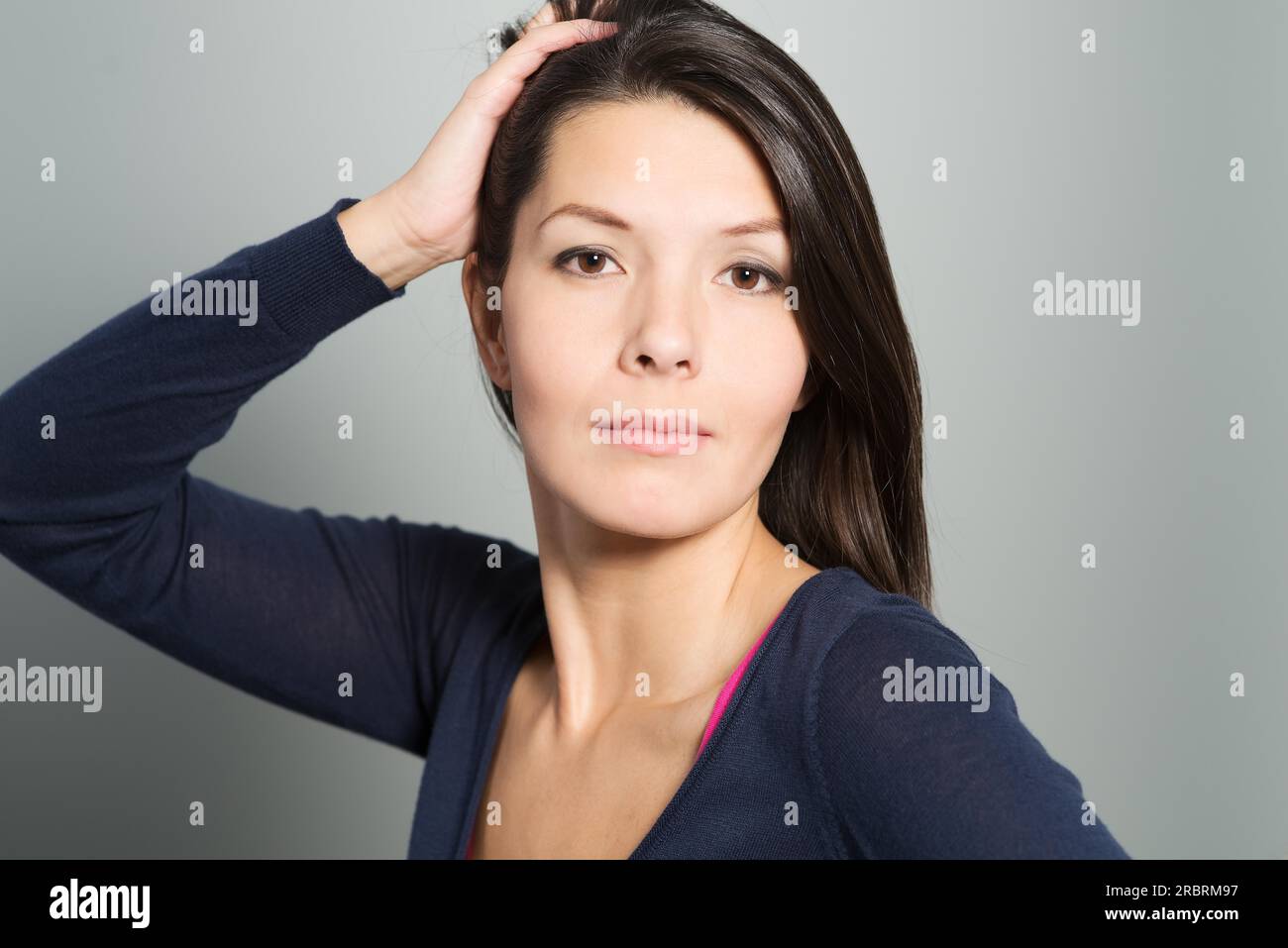 Thoughtful attractive woman with a serene face and enigmatic smile standing with her hand to her chin looking pensively at the camera Stock Photo