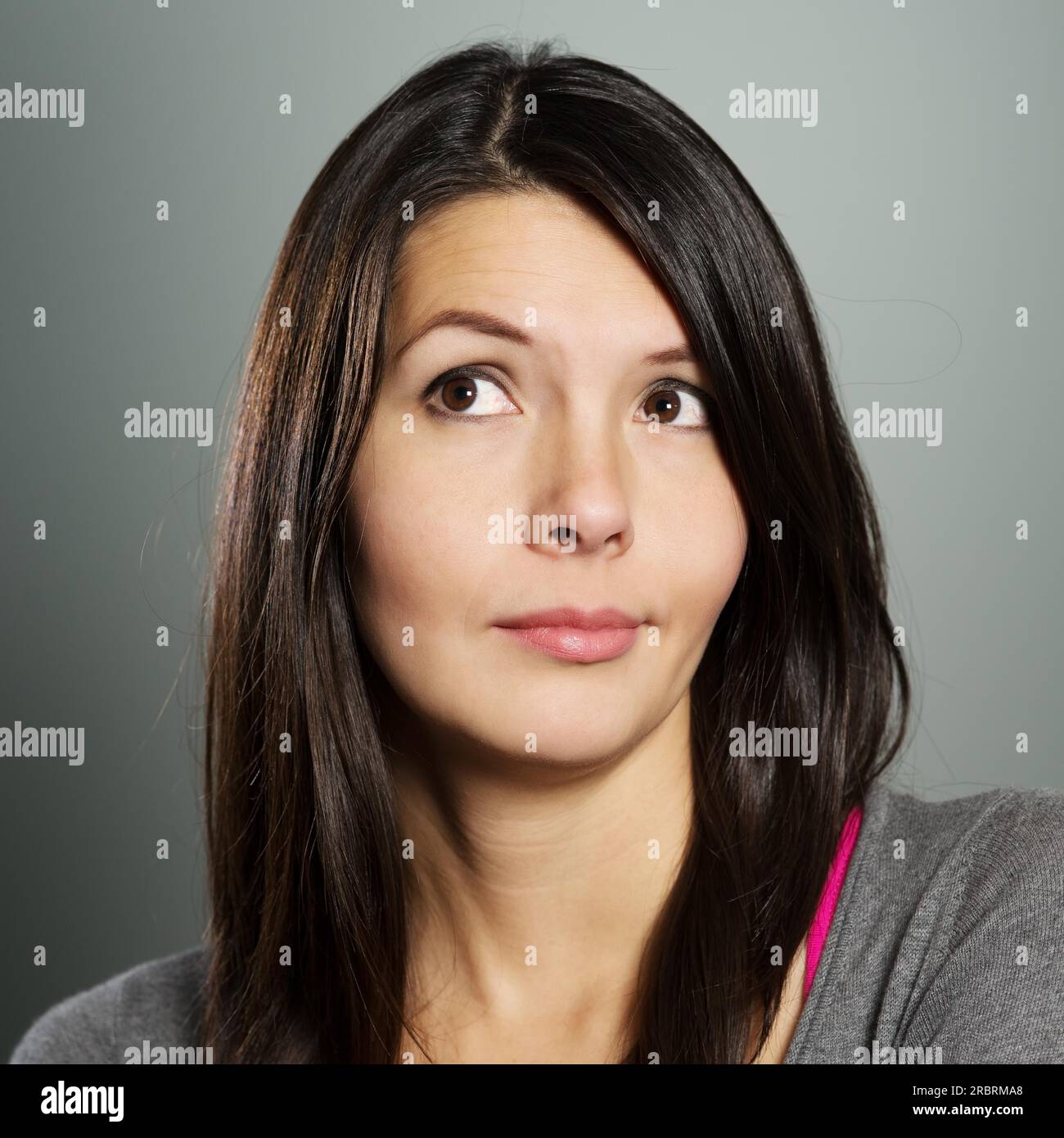 Attractive woman with a sceptical bemused expression standing with folded arms pulling a wry face as she looks upwards into the air Stock Photo