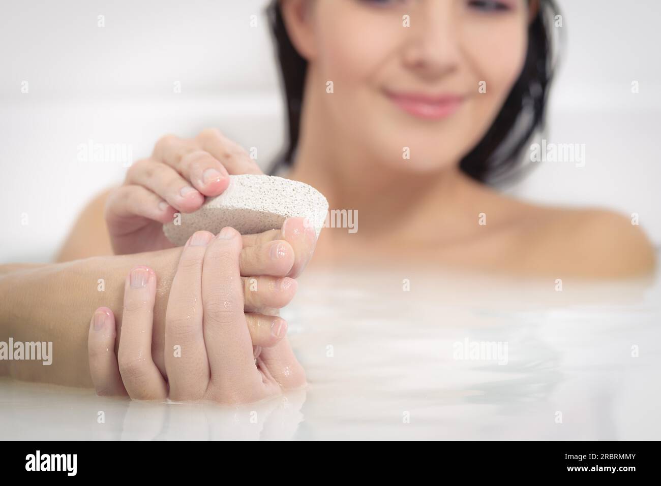 Woman relaxing in a hot soapy bath using a pumice stone to exfoliate her feet and remove dead skin cells from the sole in a personal hygiene and Stock Photo