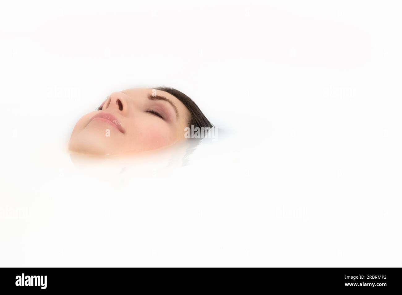 Blissful beautiful young woman pampering herself soaking in a hot bath with just her face visible above the soapy water as she relaxes with a serene Stock Photo