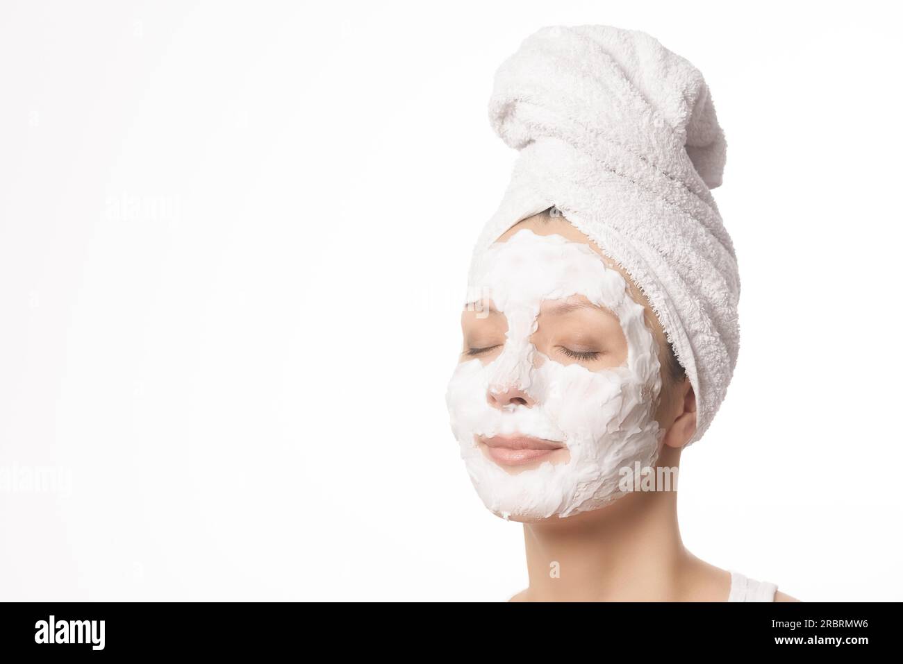 Relaxed woman with her hair tied up in a white towel and a deep cleansing nourishing face mask applied to her face, beauty and skincare concept Stock Photo