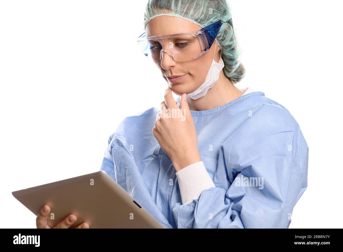 Attractive female surgeon or doctor in a mask goggles and surgical gown standing consulting a tablet computer reading the information with a serious Stock Photo
