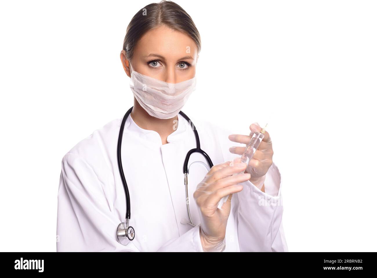 Female doctor or anaesthetist in a gown and mask fitting a needle to a hypodermic syringe to administer an anaesthetic or medication, isolated on Stock Photo