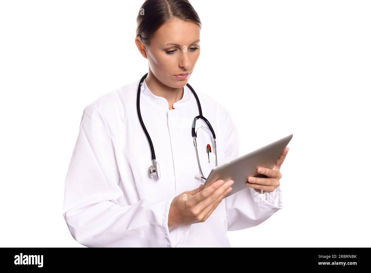 Attractive female nurse or doctor in a white gown standing consulting a tablet computer reading the information with a serious expression, isolated Stock Photo