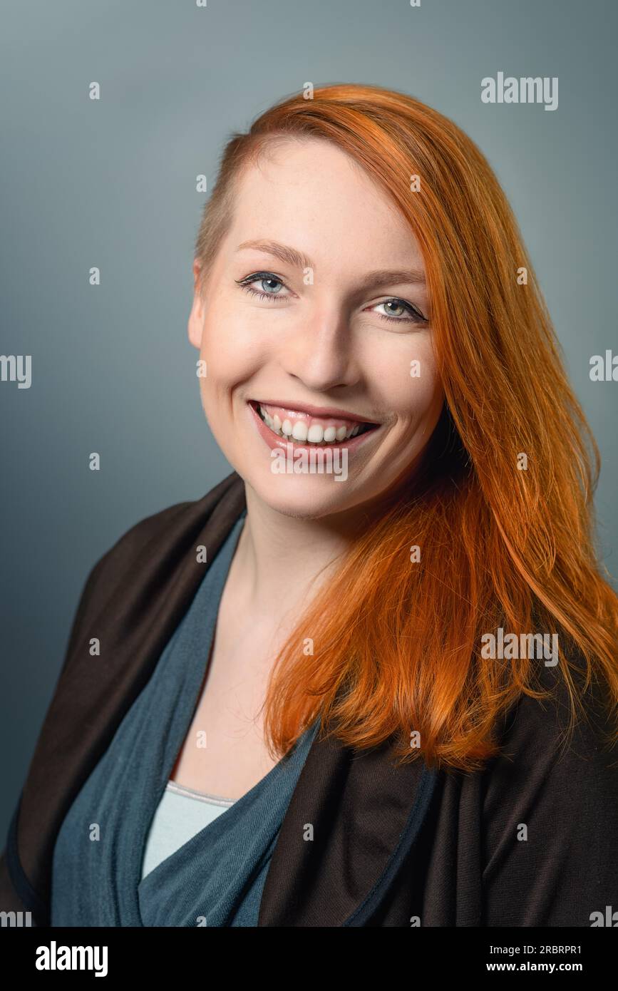 Portrait of Smiling Confident Red Haired Woman Casually Dressed looking at the camera on gray studio background Stock Photo