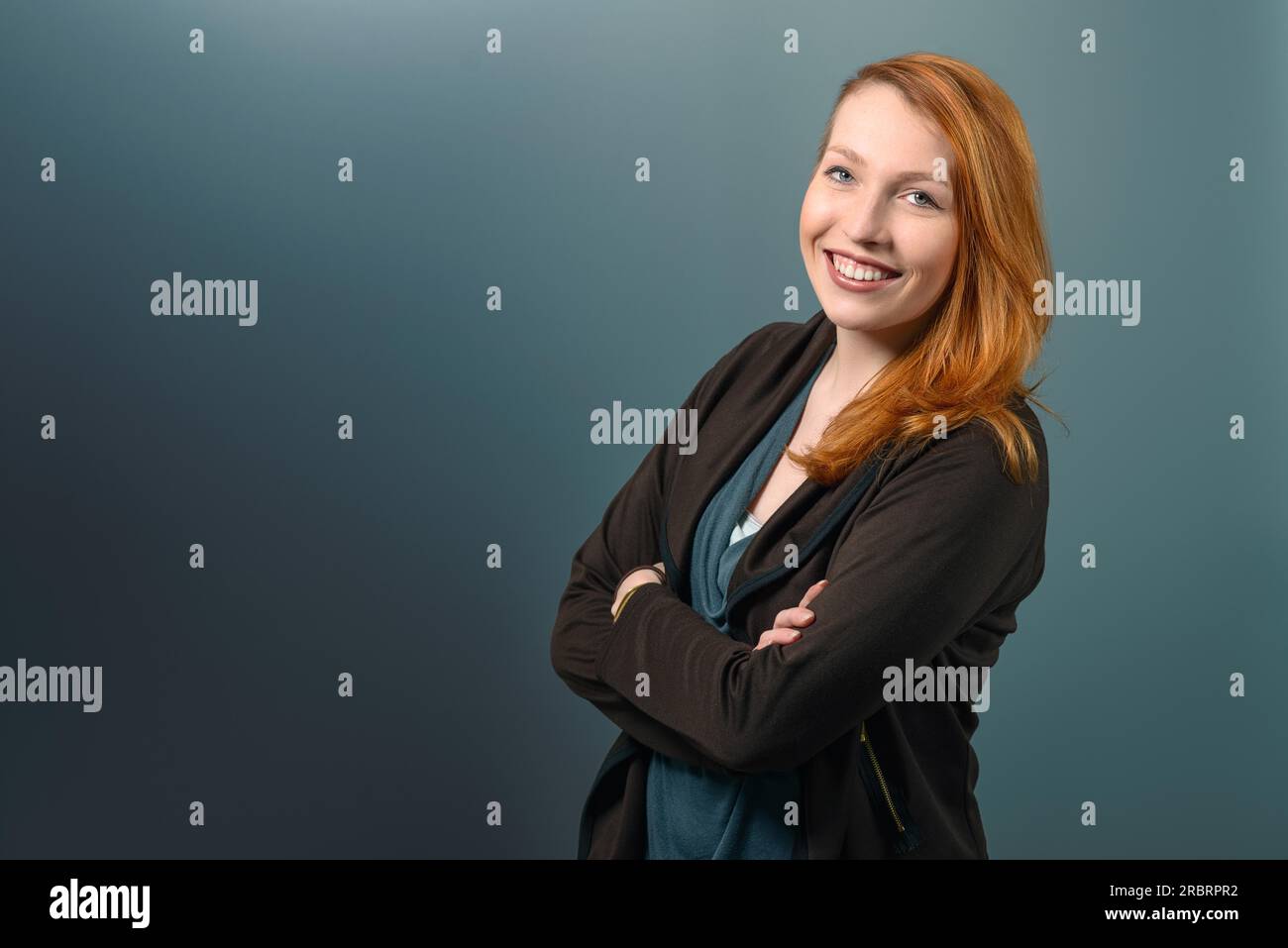 Portrait of Smiling Confident Red Haired Woman Casually Dressed with Arms Crossed in Studio with Grey Background Stock Photo