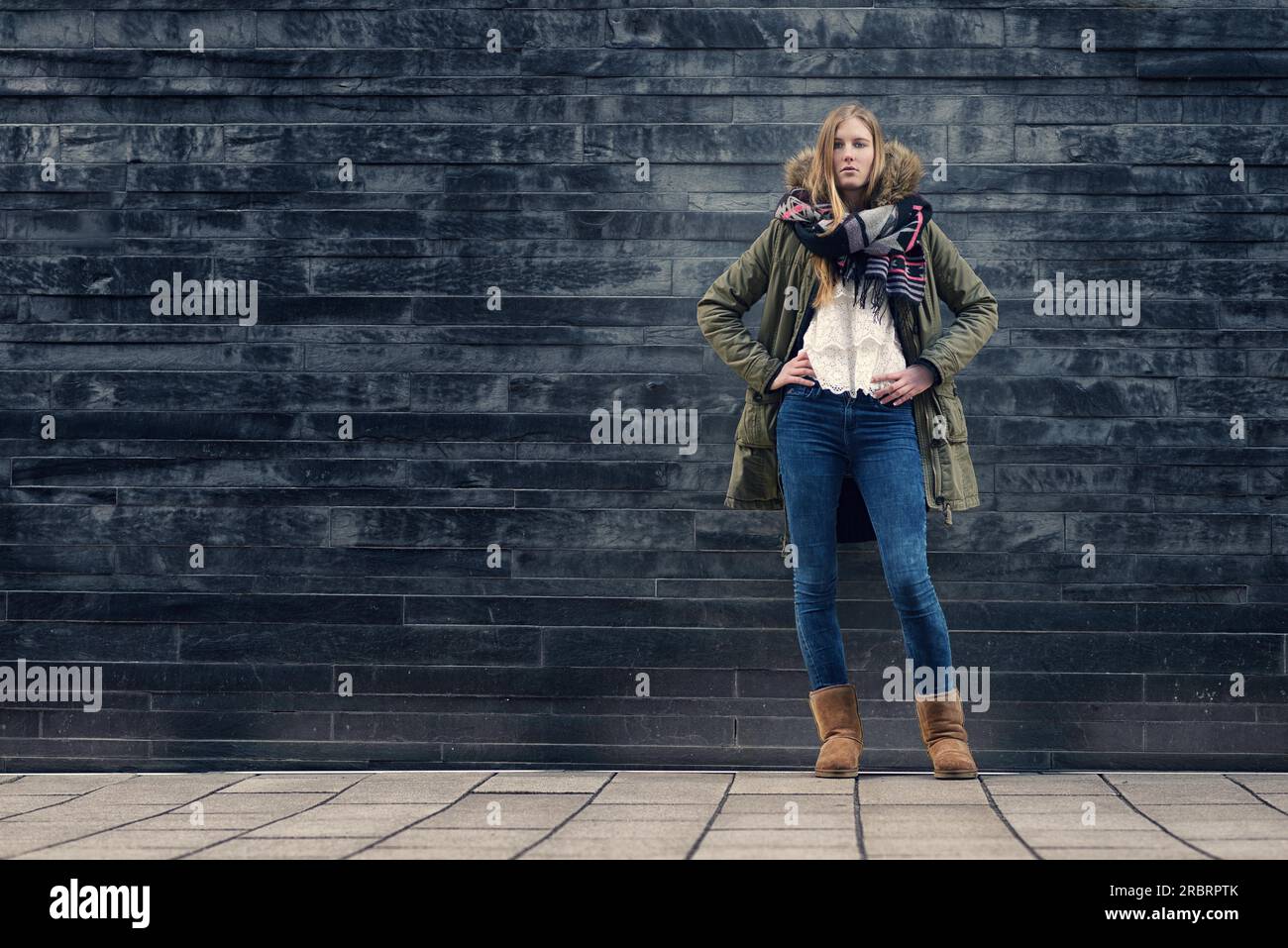 Fashionable Young Woman in Winter Outfit Posing in Front Old Gray Wall while Looking at the Camera Stock Photo