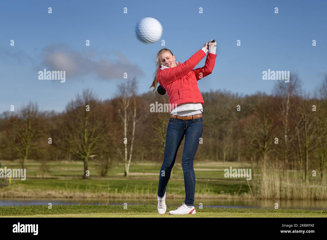 Woman golfer hitting the golf ball with a driver in front of a water