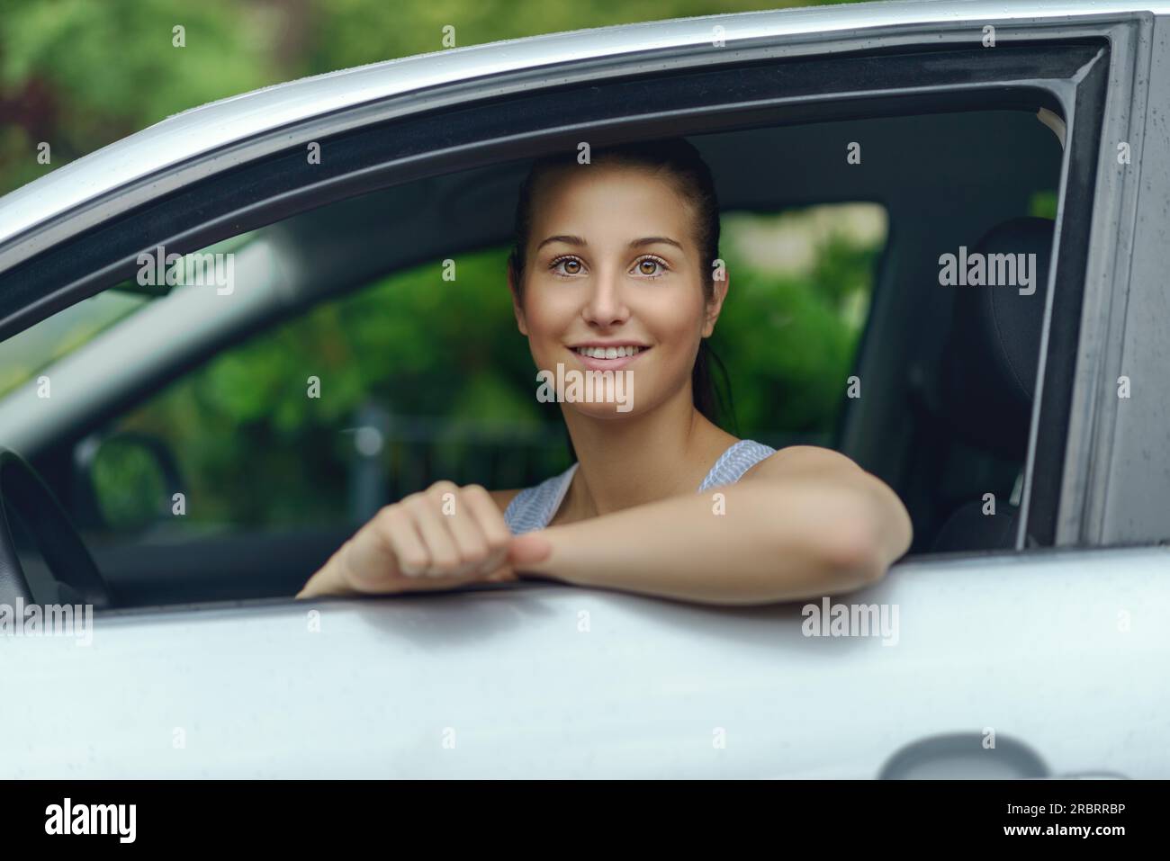 Pretty Young Woman Sitting Inside the Car, Smiling at the Camera While Leaning on the Open Window Stock Photo