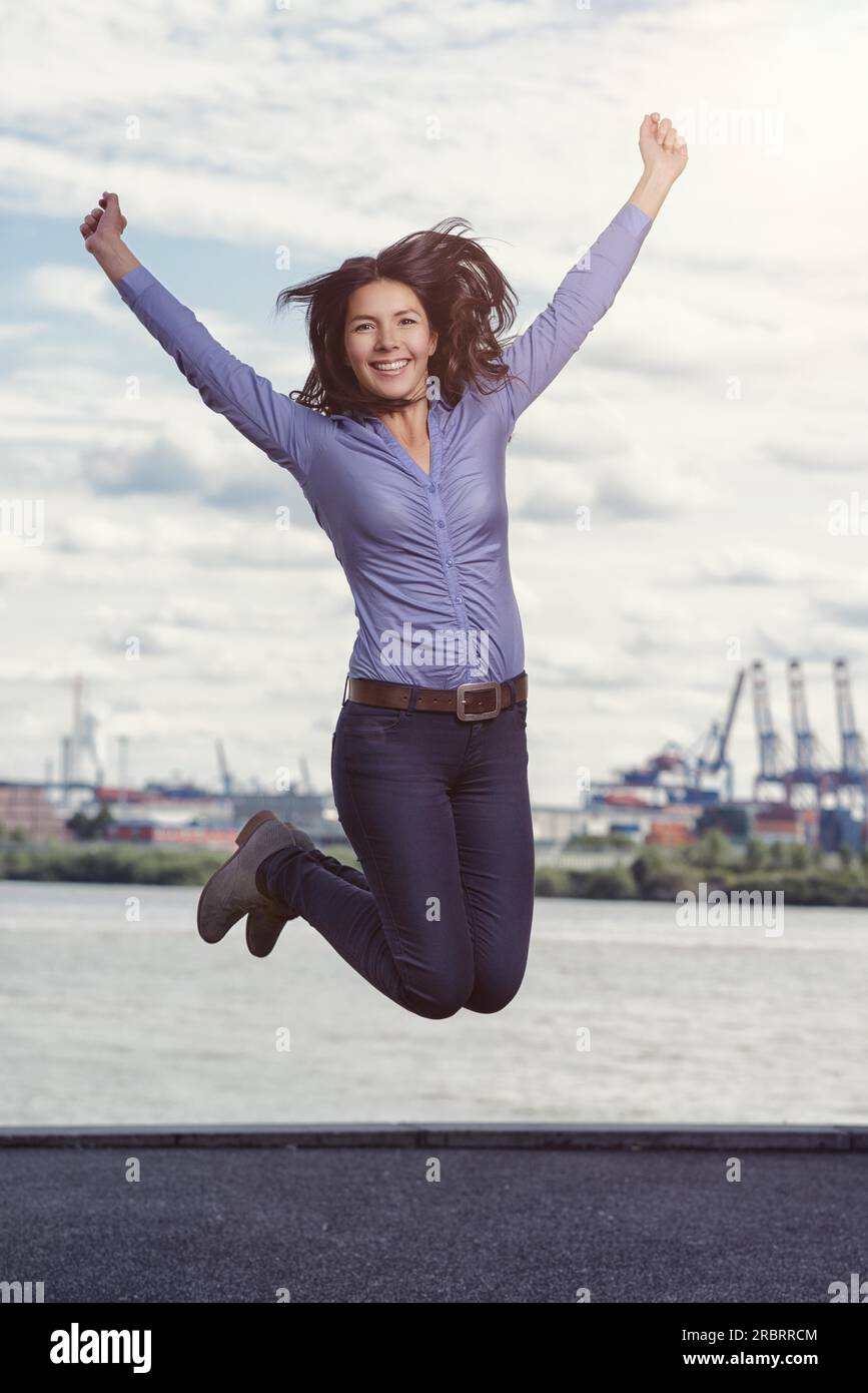 Young woman leaping and cheering for joy with her arms raised and a ...