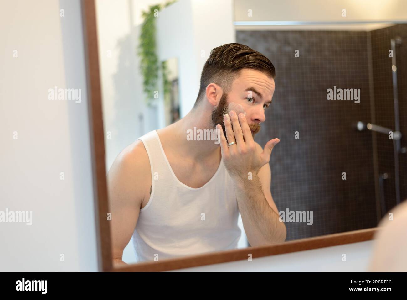 Young man applying shaving cream above his beard, morning routine, a