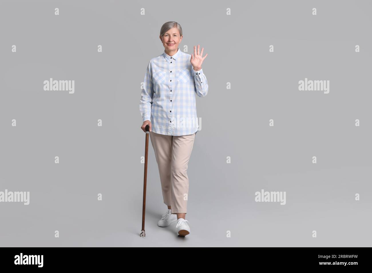 Senior woman with walking cane waving on gray background Stock Photo ...