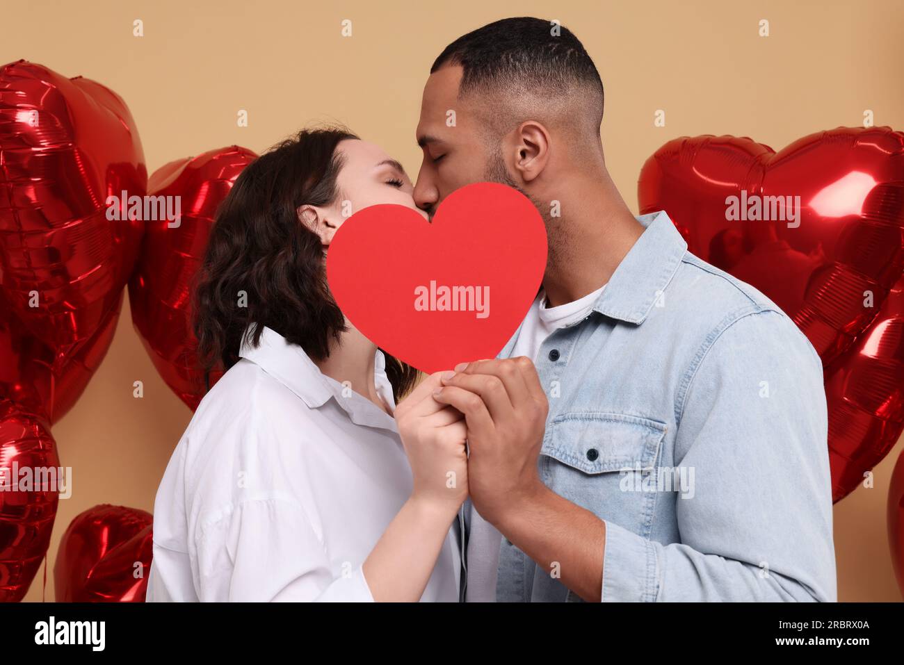 Lovely couple kissing behind red paper heart on beige background ...