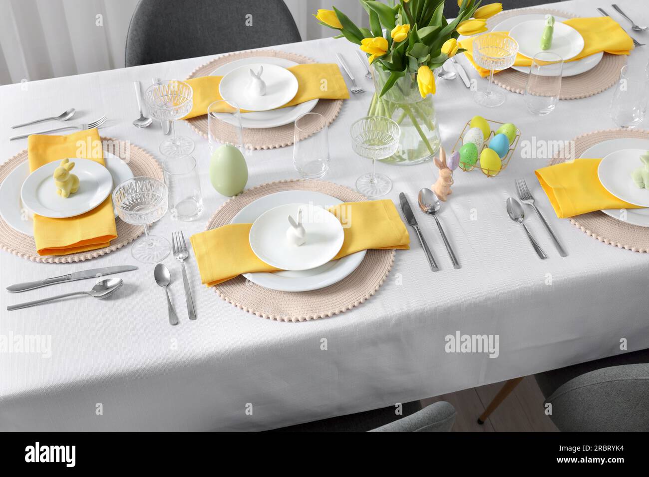 Festive table setting with glasses, painted eggs and vase of tulips ...