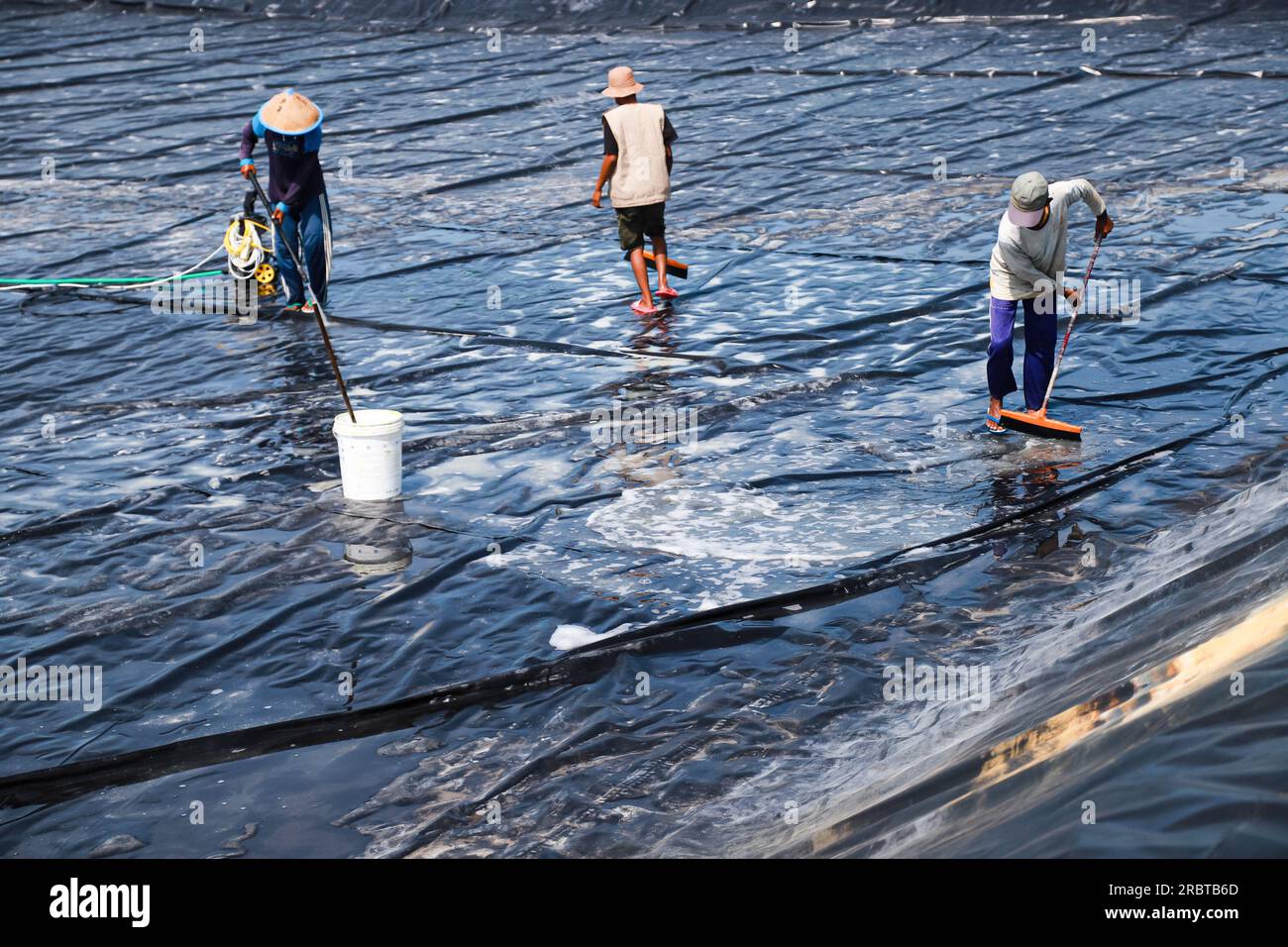 Several pond farmers are cleaning LDPE plastic ponds before starting to put water into the vanamei fish and shrimp farming ponds Stock Photo