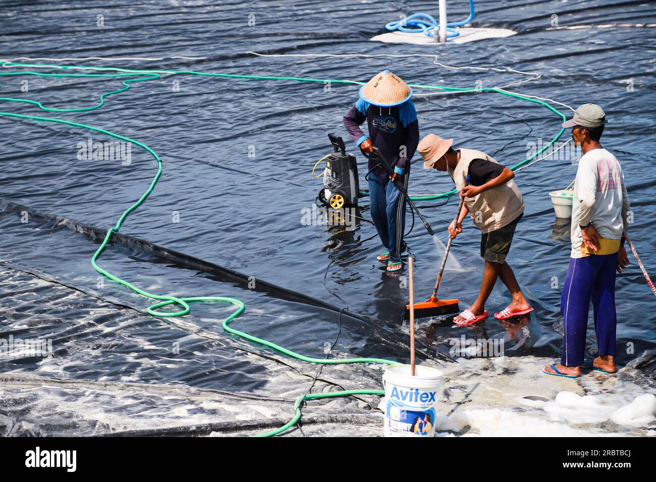 Several pond farmers are cleaning LDPE plastic ponds before starting to put water into the vanamei fish and shrimp farming ponds Stock Photo