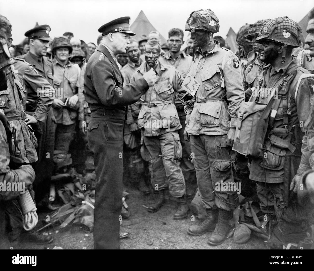 Berkshire, England:   June 5, 1944 General Dwight D. Eisenhower talking with American paratroopers on the evening of June 5, 1944, as they prepared for the Invasion of Normandy. The men are part of Company E, 502nd Parachute Infantry Regiment, at the 101st Airborne Division's camp in Greenham Common. Photo includes Sgt. Russell Wilmarth, behind Eisenhower's chin, Lt. Wallace C. Strobel with a '23' tag, Ralph 'Bud' Thomas, to the left of Strobel, (and probably Corporal Donald E. Kruger, in front row, far right, wearing a musette bag on his chest Stock Photo