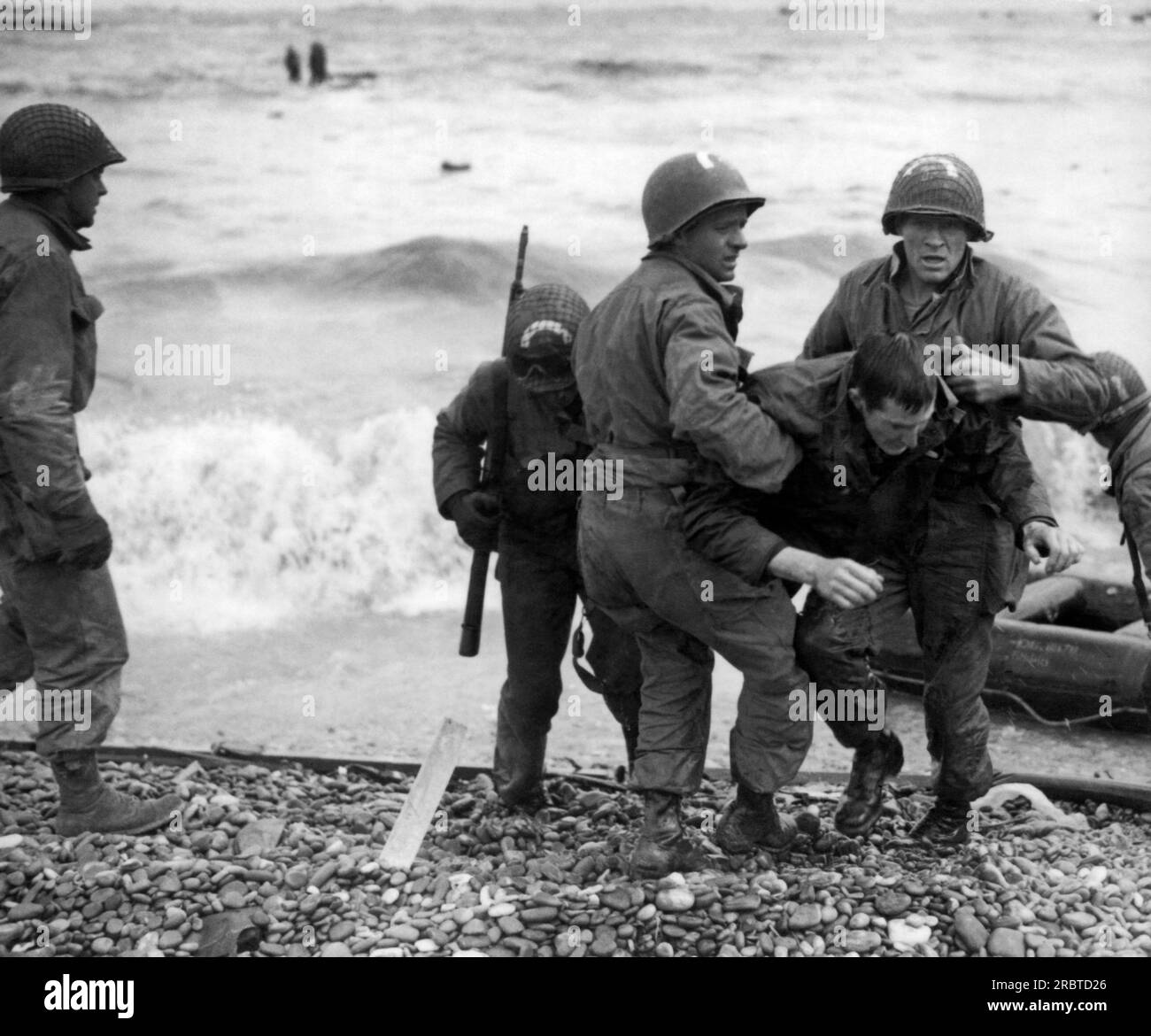 Normandy, France:  June 6, 1944 Survivors of a sunk LCVP off the coast of France are helped ashore from a rubber life raft at Omaha Beach. Stock Photo