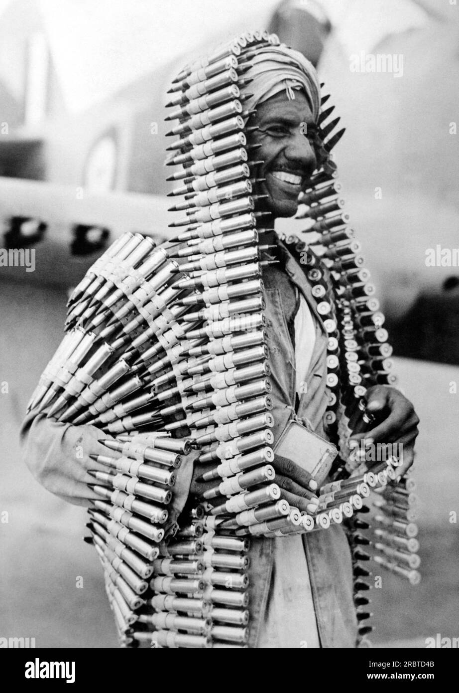 Libya:  c. 1941 An Arab assistant to an R.A.F. armourer pleased with this original head-dress of ammunition for a 'Kittyhawk' fighter plane against the German convoys in Africa.. Stock Photo