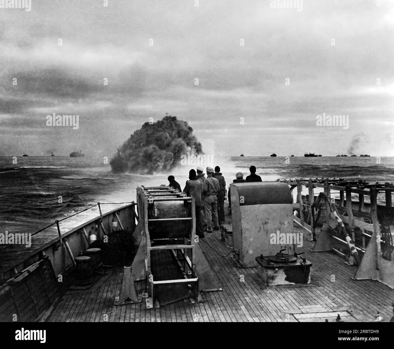 Atlantic Ocean, 1943 Coast Guardsmen on the Cutter 'Spencer' watching their depth charge explosion that blasted a Nazi U-Boat hoping to attack the convoy in the background, to the surface where it was engaged by the Coast Guard Cutter 'Spencer'. Stock Photo
