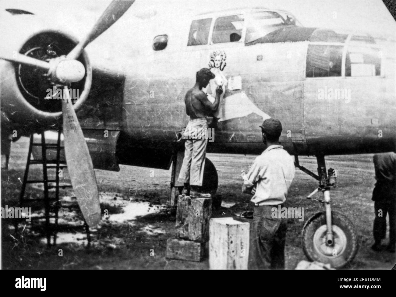 Australia:  c. 1943 A 5th AAF airman artist painting a pin-up on the nose of a B-25 bomber of the 80th Bomber Group stationed in Australia. Stock Photo