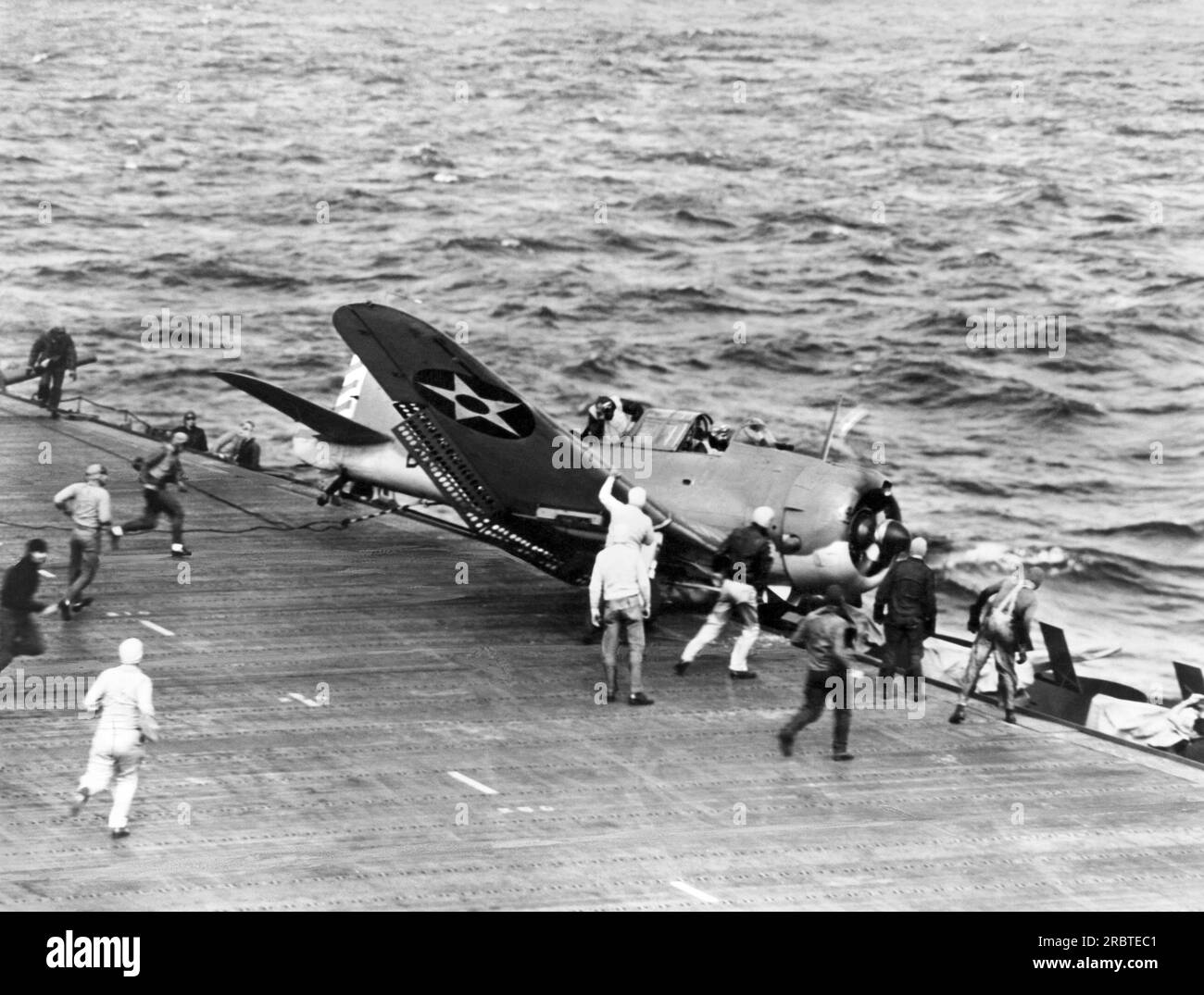 Pacific Ocean:  August, 1942 U.S. Navy scout bomber crashes while landing on the aircraft carrrier flight deck and ends up in the catwalk as ground crews rush to assist. Stock Photo