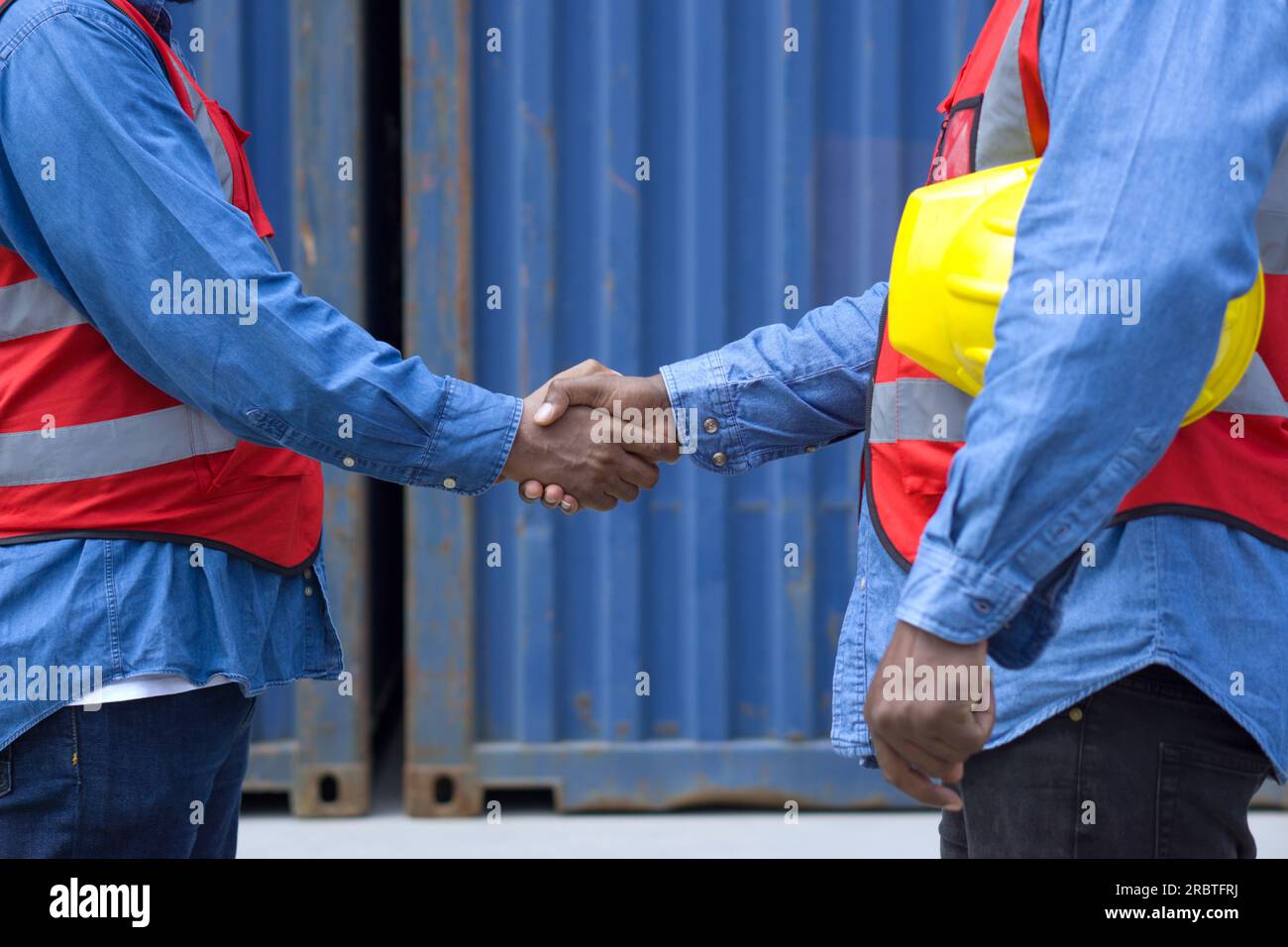 Two workers clad in safety helmets and reflective vests shake hands in ...