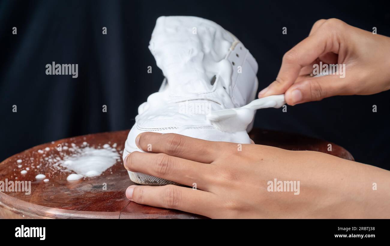 A Woman cleaning white leather shoes with cleaning foam. The concept of