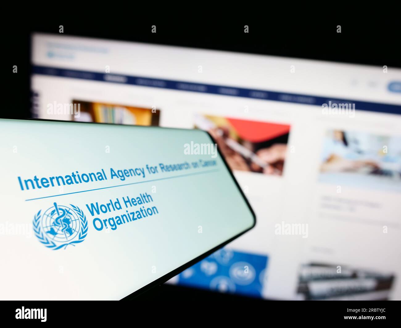 Mobile phone with logo of International Agency for Research on Cancer (IARC) on screen in front of website. Focus on left of phone display. Stock Photo