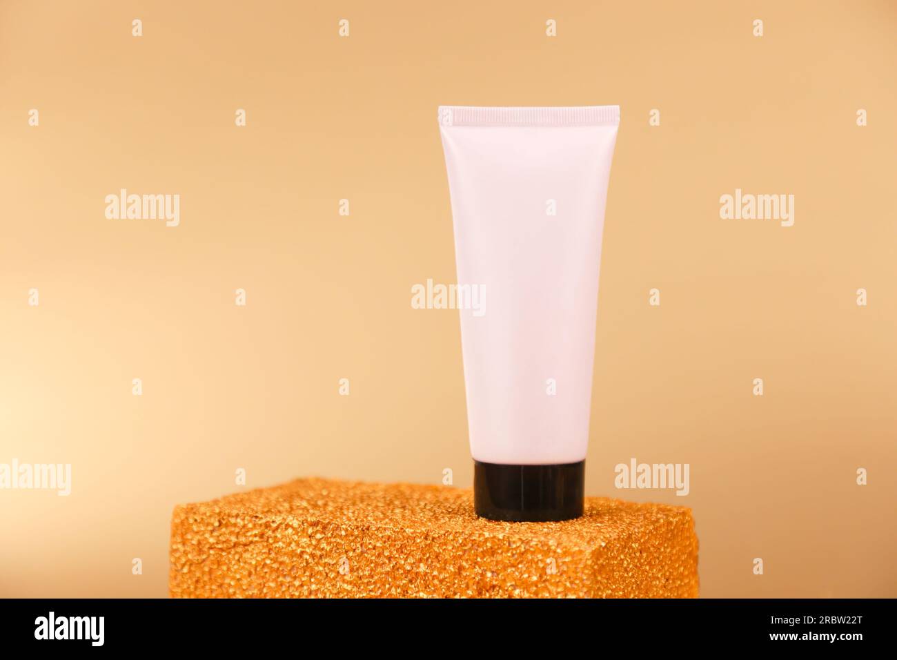 Unbranded light pink squeeze bottle plastic tube with black screw cap on golden podium on gold background. Front view, mockup. Natural organic spa cos Stock Photo