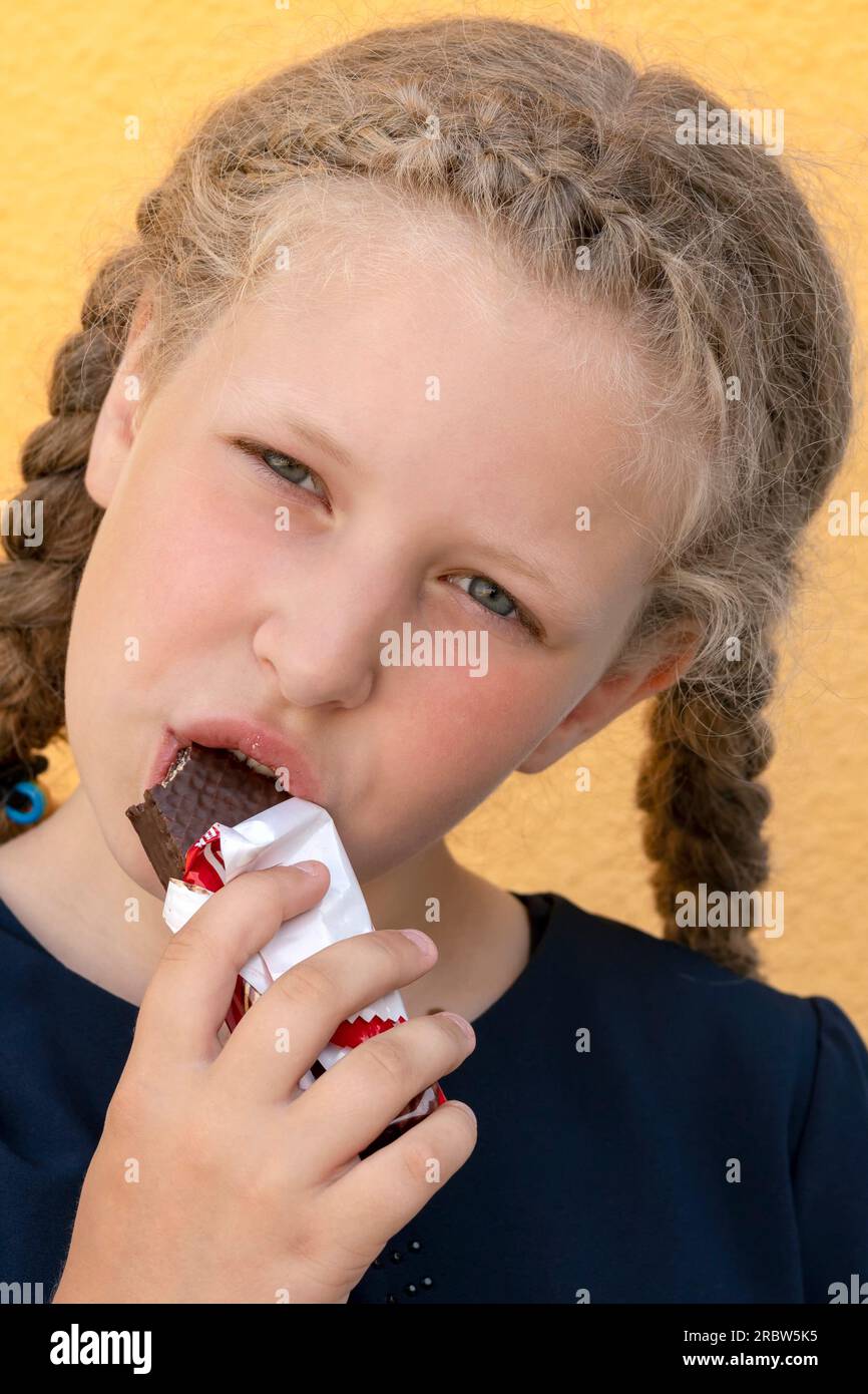 Girl eating a chocolate bar closeup. Portrait of a  schoolgirl on the background. Concept  school meals. girl with a chocolate bar. pupil with a stick Stock Photo