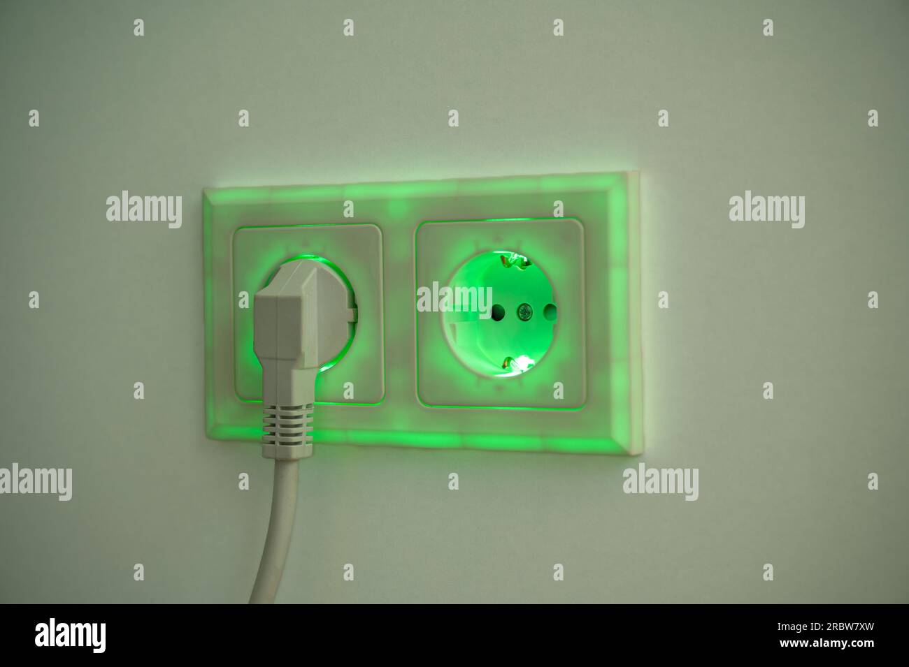 Green illuminated socket with plug inserted to symbolise power consumption and electrical energy
