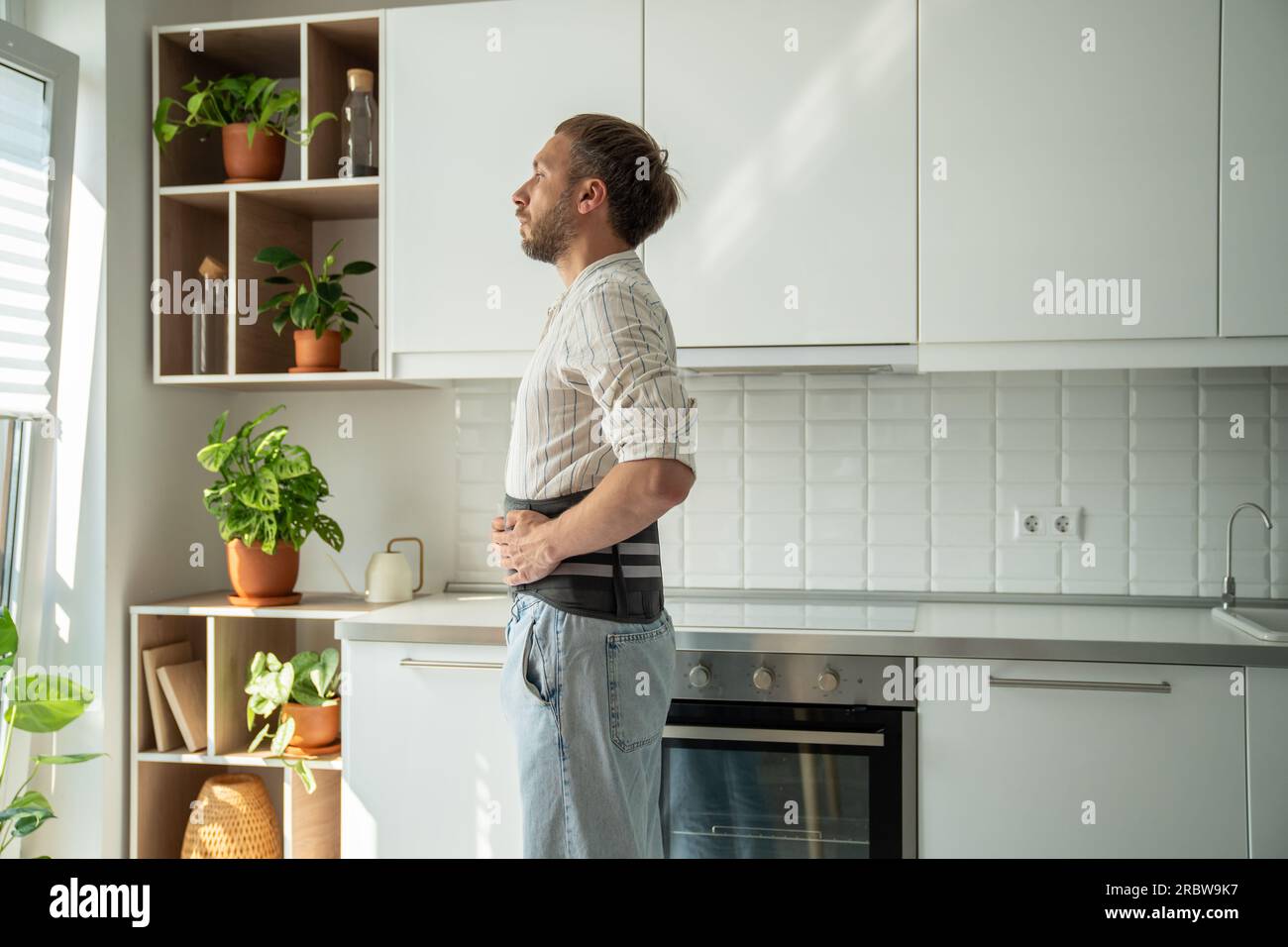 Young man wearing lumbar corset brace looking out window at home Stock Photo