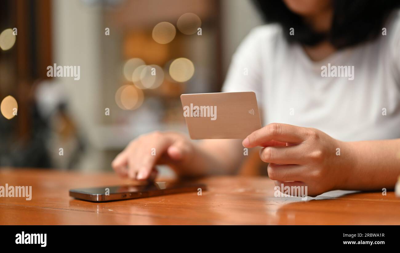 Close-up image of a young Asian woman holding a credit card and using her smartphone to register online payment on a shopping app. Stock Photo