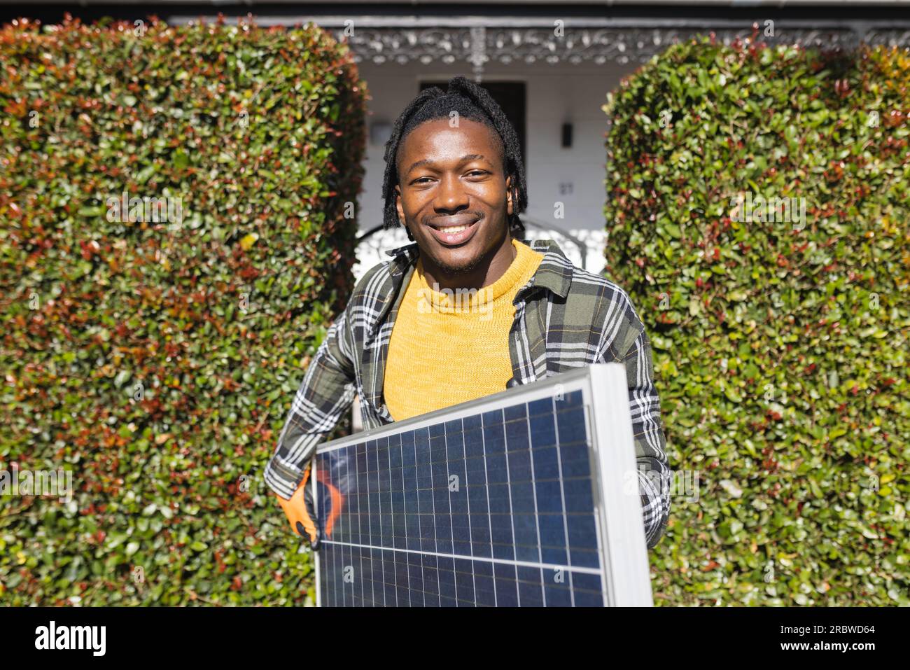 Portrait of happy african american man holding photovoltaic solar panel in front of house Stock Photo
