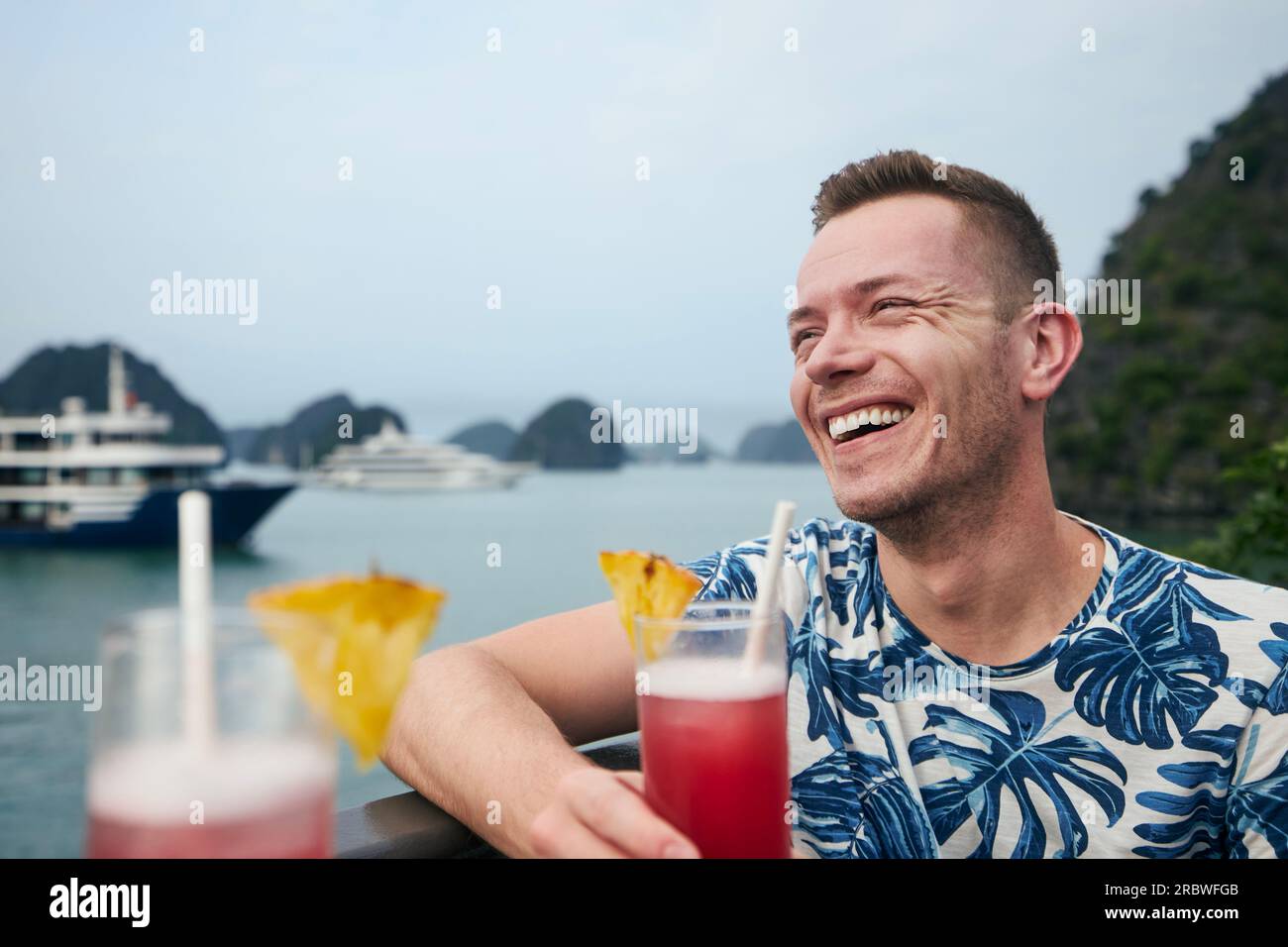 Portrait of smiling man with coctail drink in hand while. Traveler enjoying cruise on boat. Travel destination Ha long Bay, Vietnam. Stock Photo