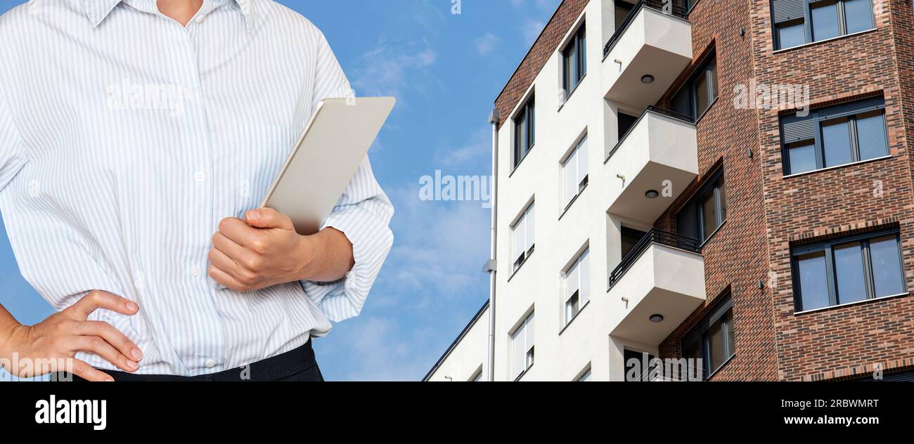 Woman real estate agent holding digital tablet in hand on background of new apartment buildings. Stock Photo