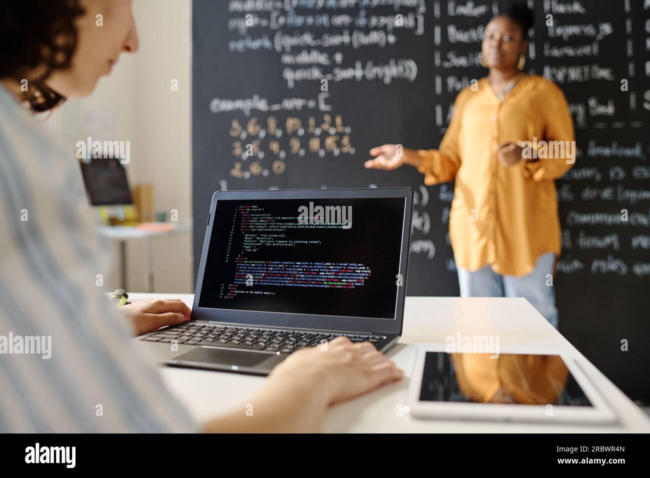 Rear view of student sitting at desk and typing codes on laptop during IT lesson Stock Photo